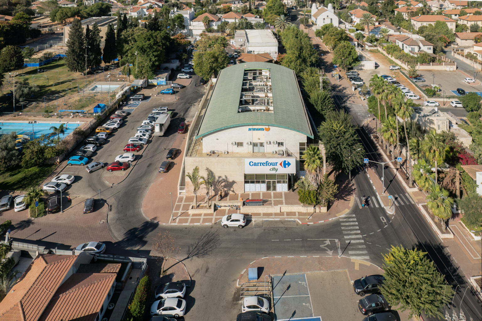 צילום חוץ של מבנה, עם שלט ״מאוחדת״ ושלט ״carrefour city״ עם כבישים, בתים, מכוניות חונות